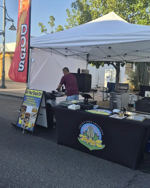 The Triple C canopy tent and logo table set up on a sunny street, with a red corn dogs flag beside it.